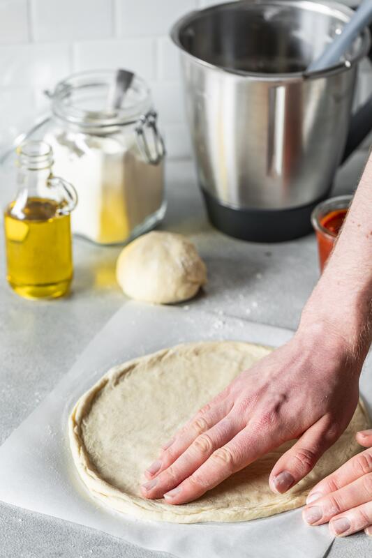 Hände streichen einen Pizzateig glatt