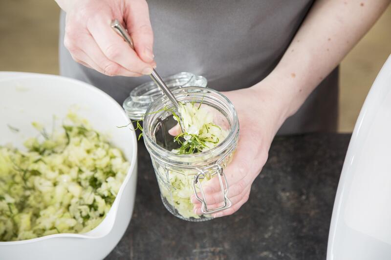 Eine Hand hält ein Glas, die andere füllt Sauerkraut hinein