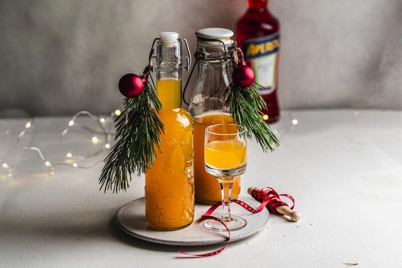 Zwei Flaschen orangefarbenen Likörs mit Tannenzweigen, daneben ein Glas