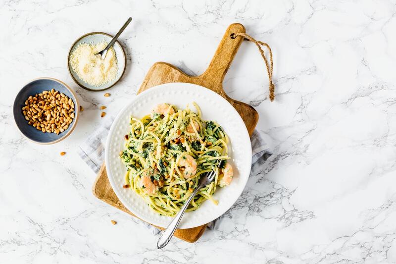 Spaghetti mit Garnelen auf einem weißen Teller von oben fotografiert, daneben eine Schale mit Pinienkernen und Parmesan