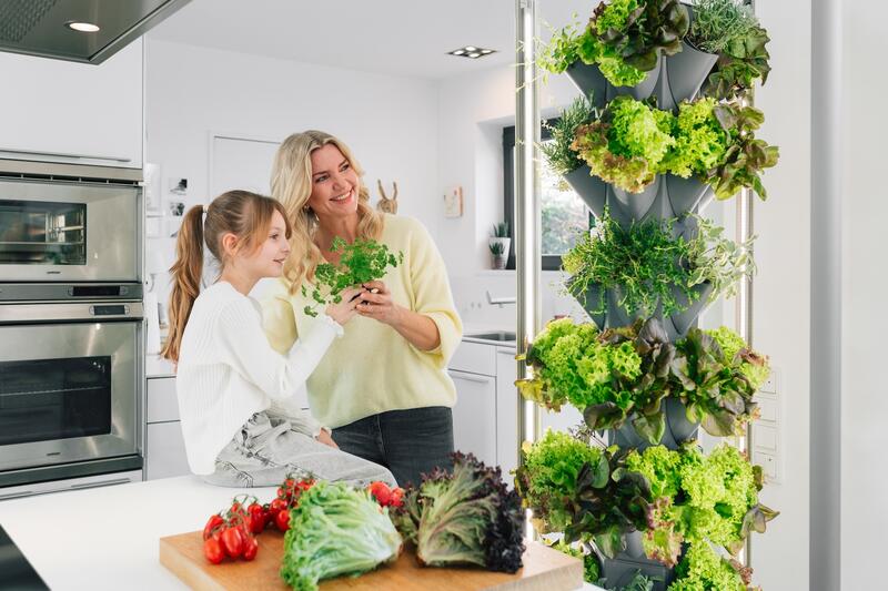 Eine Frau und ein Mädchen neben dem Greeny voller Kräuter und Salat