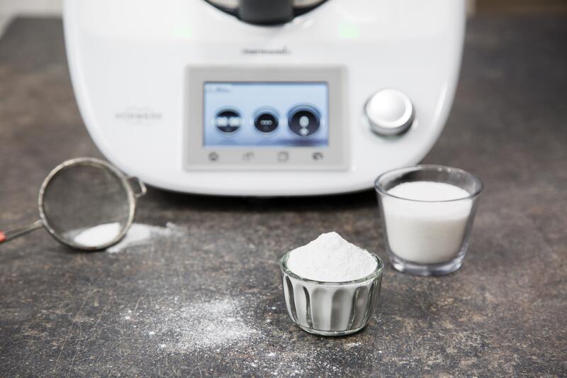 Zwei kleine Gläser mit Puderzucker vor einem Thermomix® auf grauem Untergrund