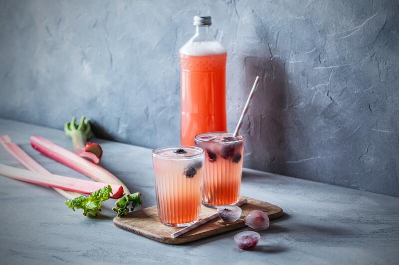 Eine Flasche und zwei Gläse mit roter Flüssigkeit und angelegten Rhabarberstangen