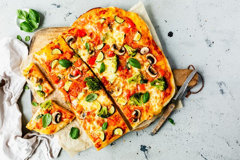 Bunt belegte Pizza vom Blech auf Holzbrett